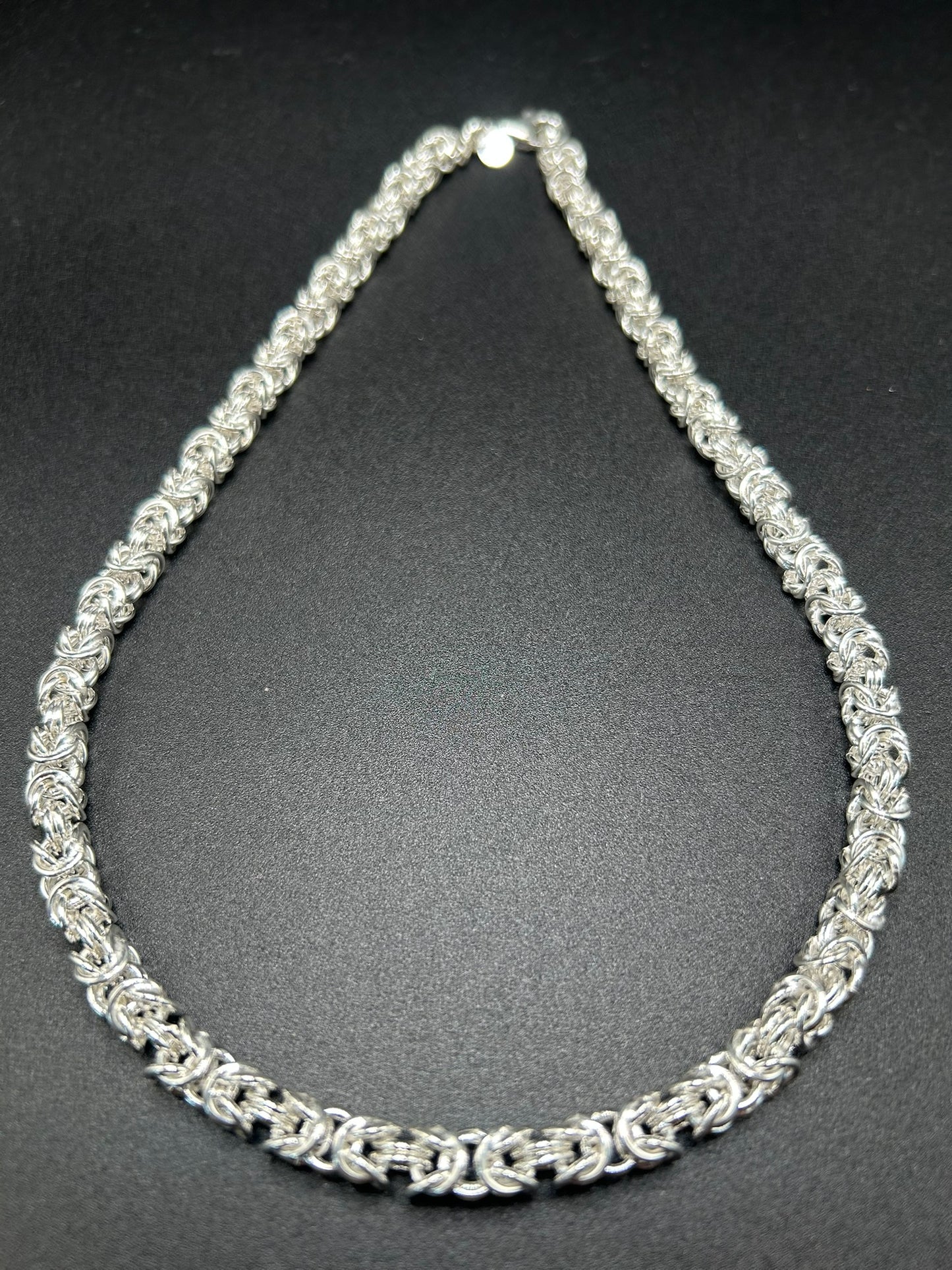 Argento che sembra intrecciato come un tessuto. Questa collana nasce dalla lavorazione della maglia bizantina, una successione articolata di anelli che crea una struttura compatta, morbida e tridimensionale.
Il risultato è un gioiello importante ma estremamente portabile, nel quale la ricchezza della trama diventa protagonista senza bisogno di pietre o altri elementi decorativi.