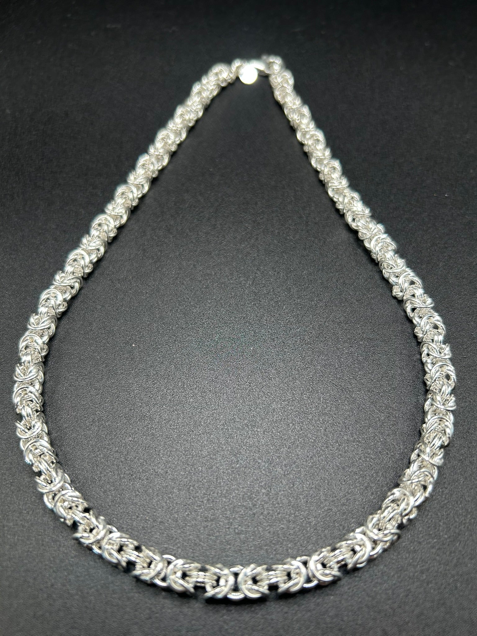 Argento che sembra intrecciato come un tessuto. Questa collana nasce dalla lavorazione della maglia bizantina, una successione articolata di anelli che crea una struttura compatta, morbida e tridimensionale.

Il risultato è un gioiello importante ma estremamente portabile, nel quale la ricchezza della trama diventa protagonista senza bisogno di pietre o altri elementi decorativi.