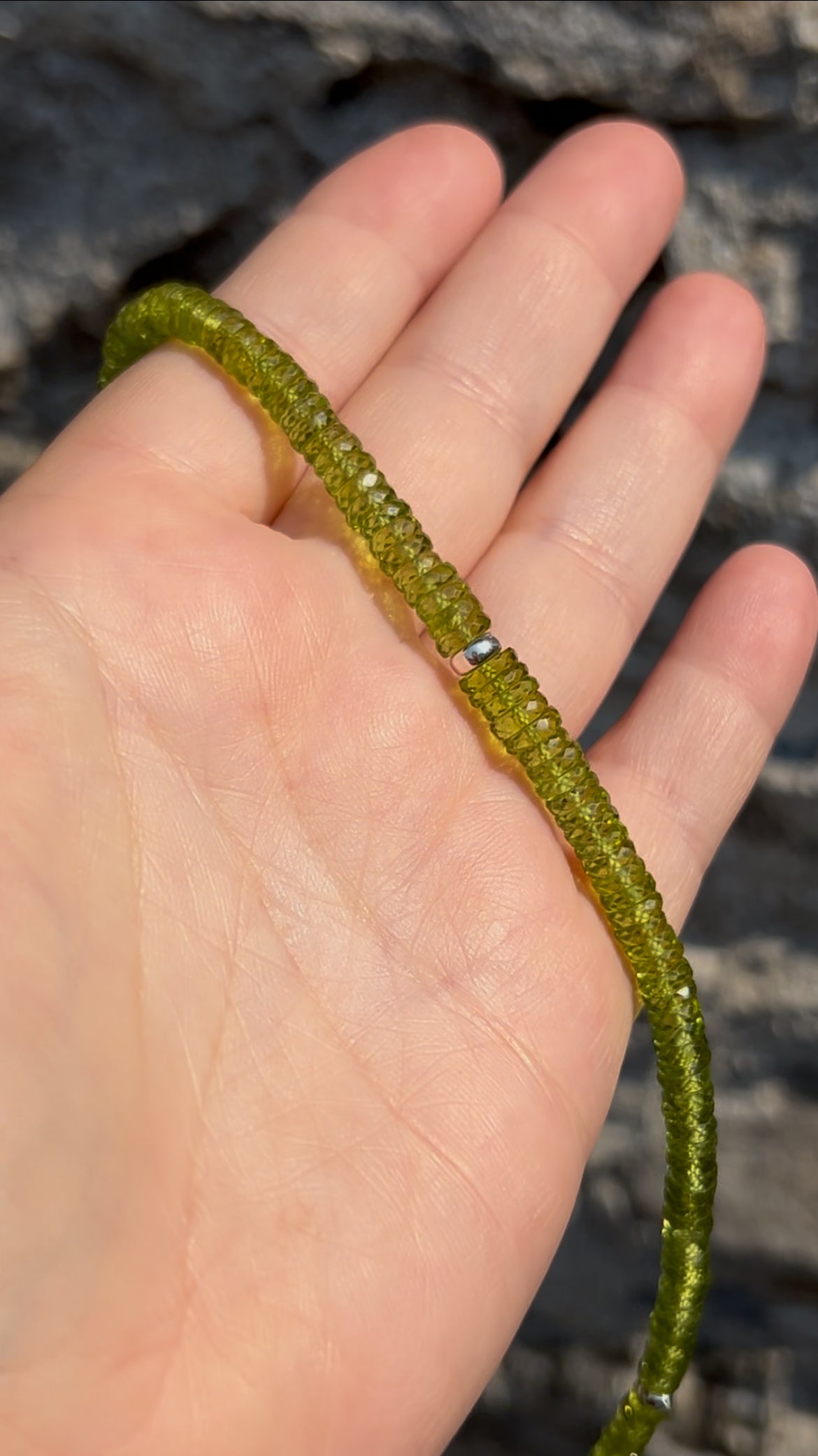 Close-up of the center section of a handmade natural peridot necklace featuring graduated faceted rondelle beads and a sterling silver 925 spacer by De Giorgi Gioielli.